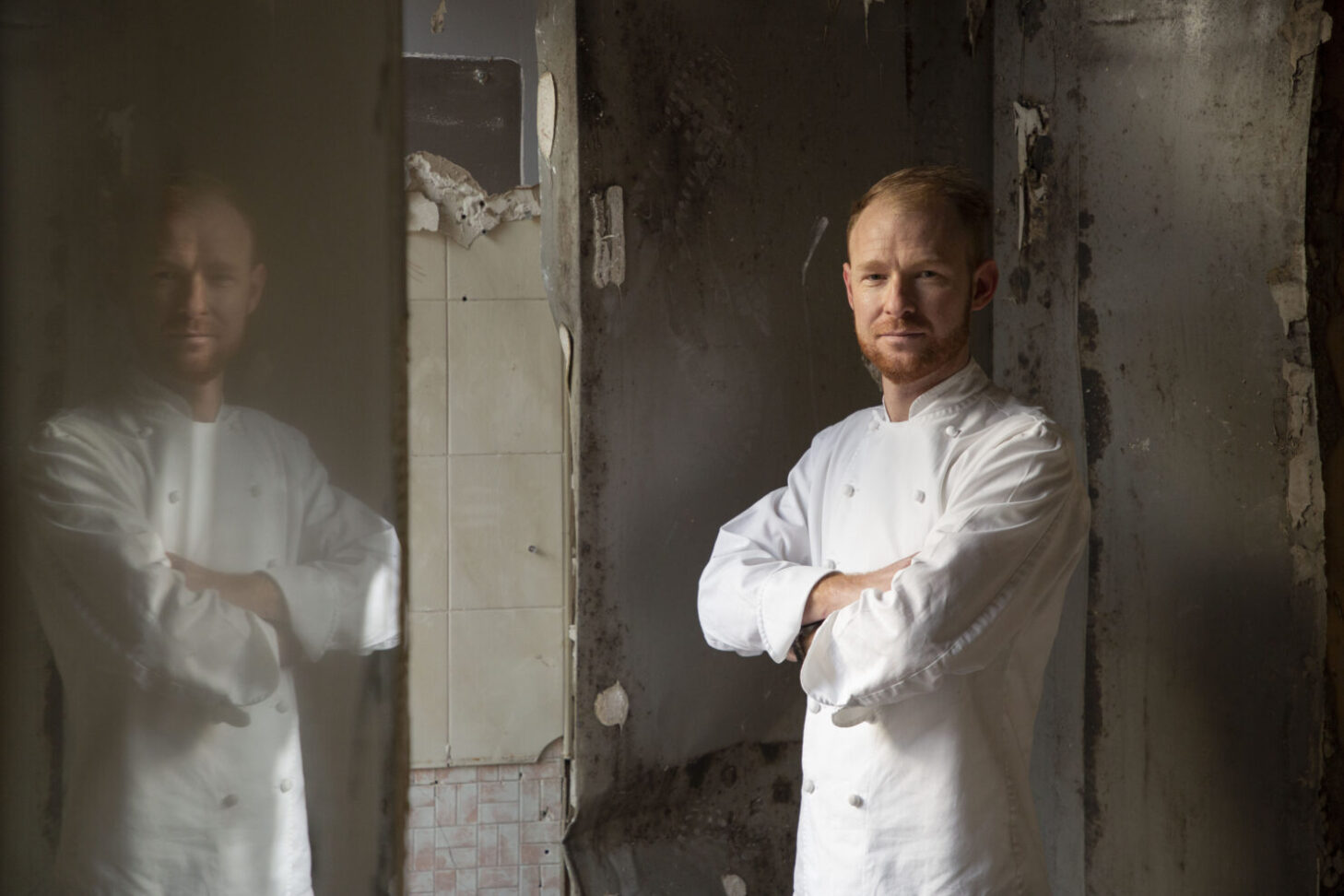 A slim middle-aged man in chef's whites stands with folded arms