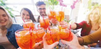 A group of young people say cheers with their aperol spritz.