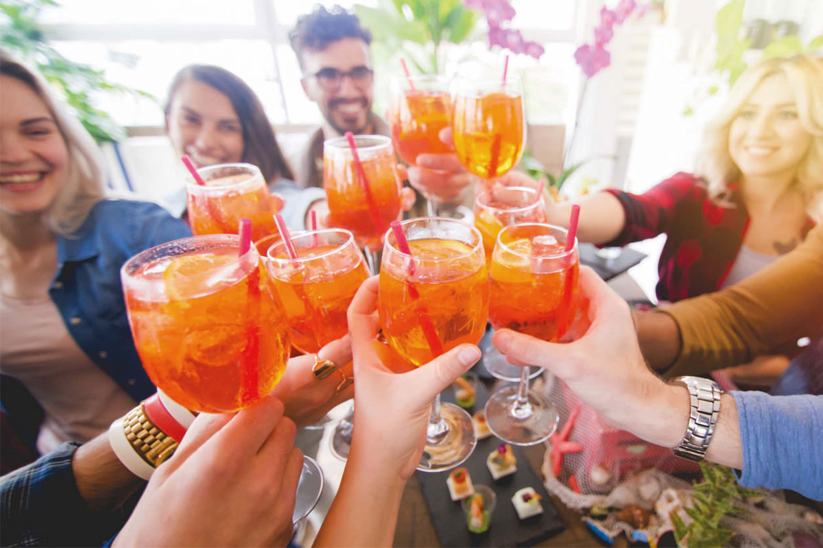 A group of young people say cheers with their aperol spritz. 