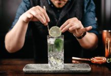 A bartender is adding a lime to a gin and tonic mix in a glass.