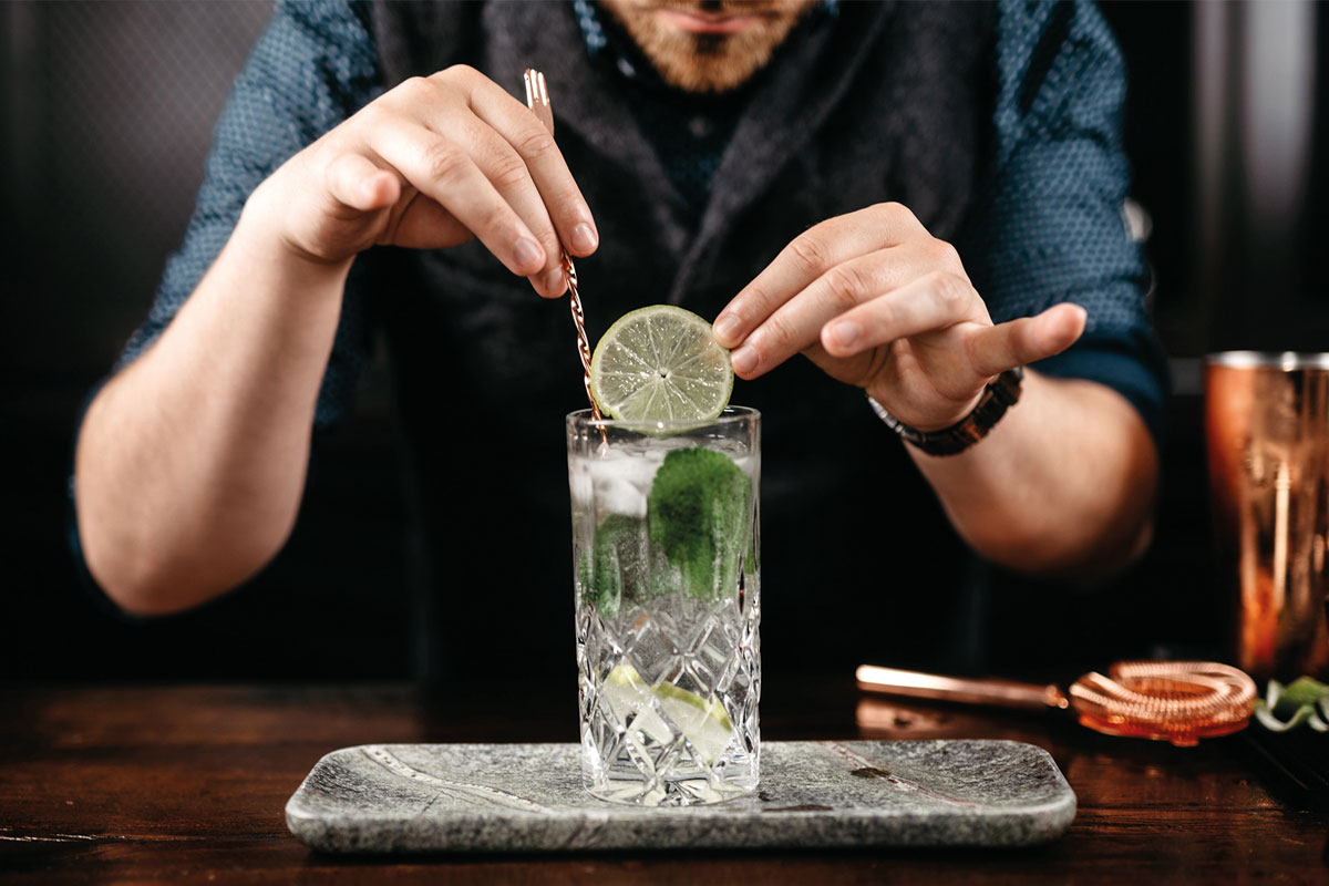 A bartender is adding a lime to a gin and tonic mix in a glass. 