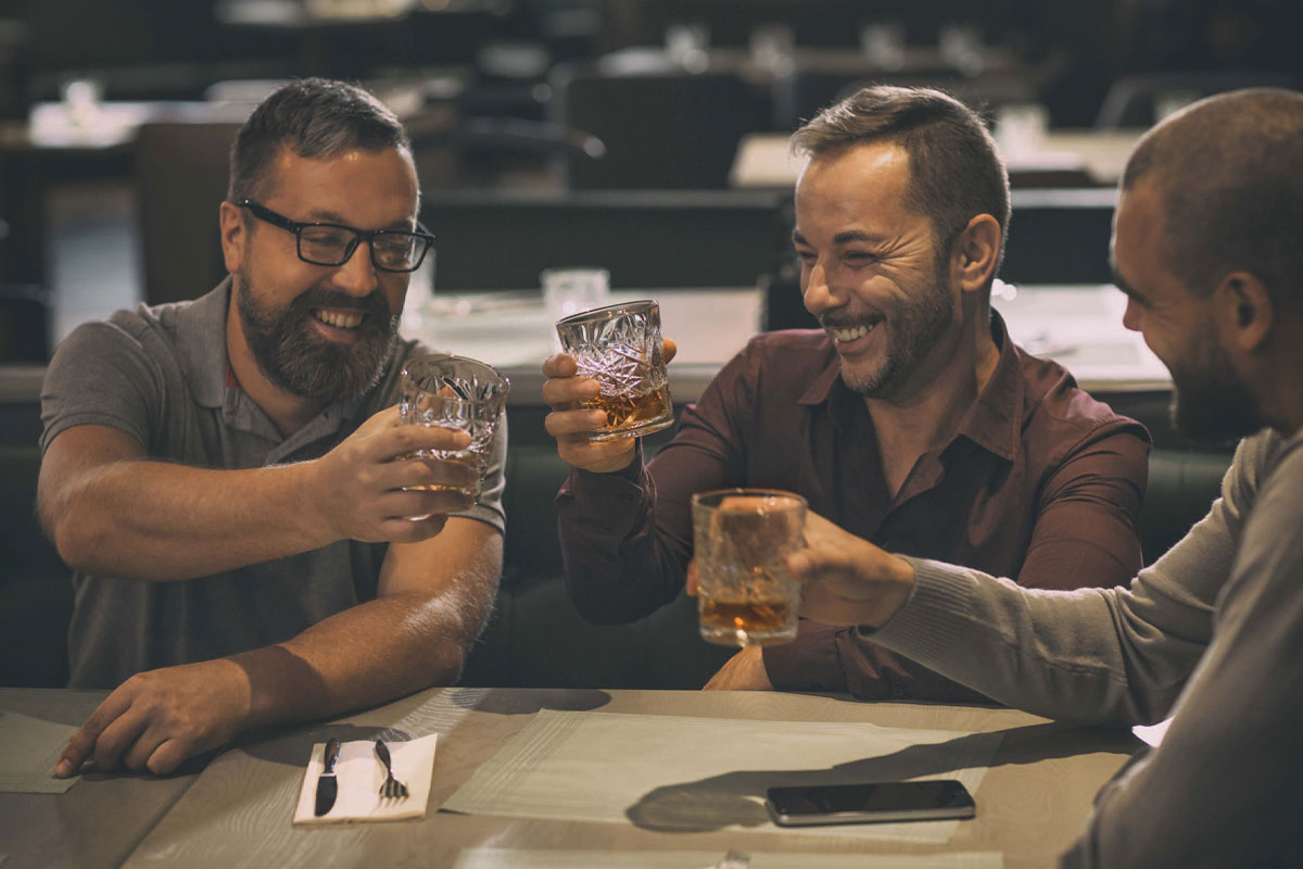 Three men cheers with glasses of whiskey in a pub