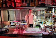 A young man stands behind a red-lit bar