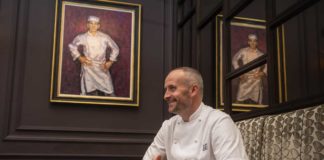 Head-Chef-Stevie-McLaughlin sits under a painting in chef whites