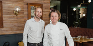 two smart looking restaurateurs stand in a well decorated restaurant