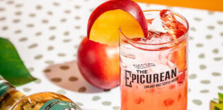 a red coloured cocktail is served in a tall glass with an apple garnish