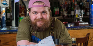 a chef wearing a pink cap and tartan apron stands with burgers and sauces
