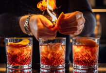 a bartended lights an orange peel garnish while making three old fashioned cocktails