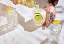 ginger beer is poured from a bottle into a glass with ice and lime