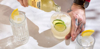 ginger beer is poured from a bottle into a glass with ice and lime