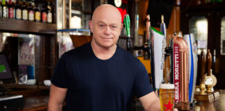 ross kemp stands behind a bar with a pint of heineken beer