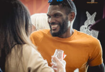 a man in an orange t-shirt smiles with a woman holding a dram glass