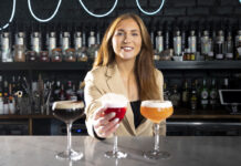 A woman in a suit sits behind three expensive looking drinks