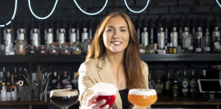 A woman in a suit sits behind three expensive looking drinks