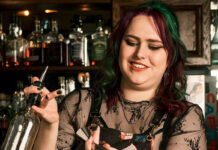 A woman with dark hair creates a complicated drink behind a bar