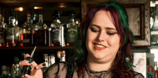 A woman with dark hair creates a complicated drink behind a bar