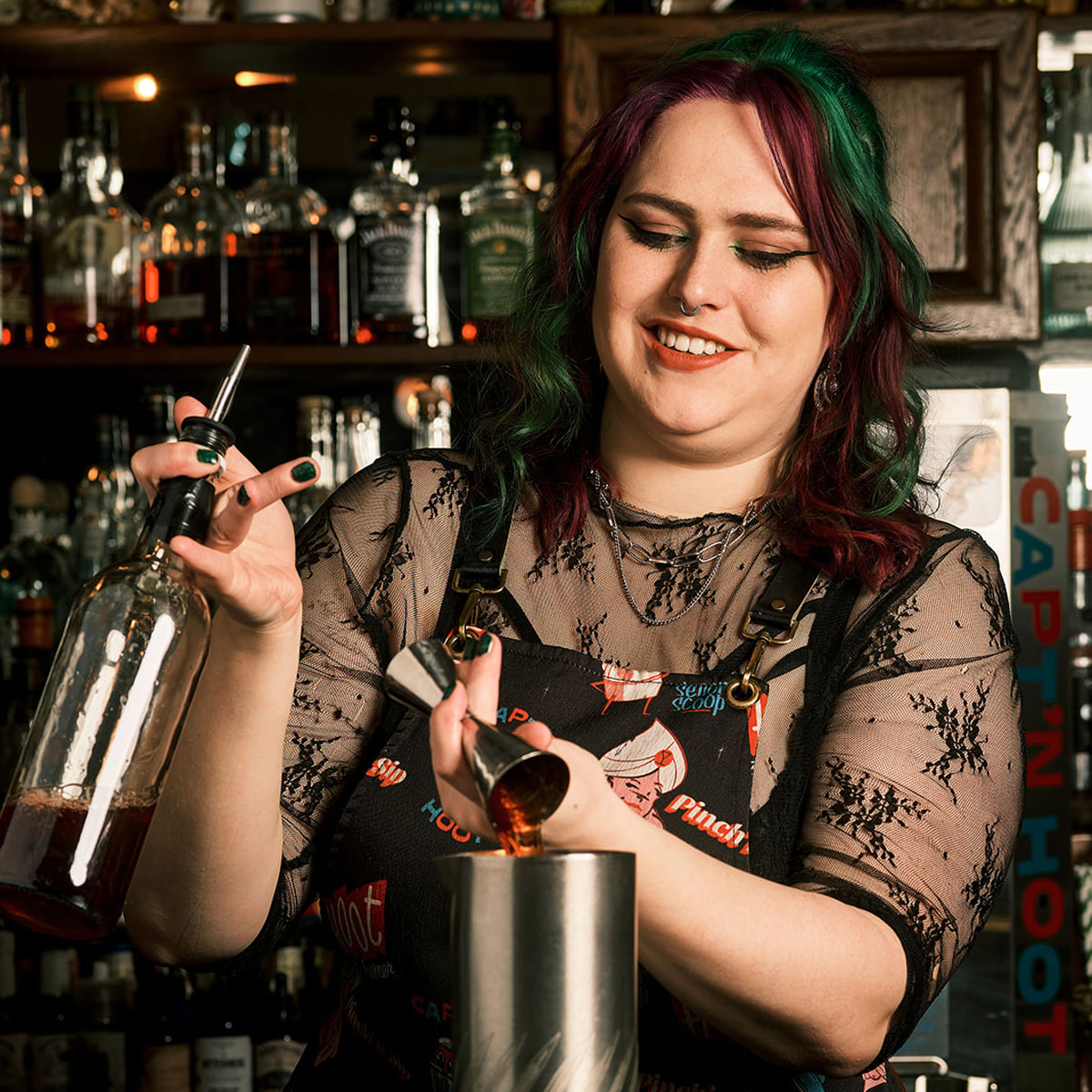 A woman with dark hair creates a complicated drink behind a bar