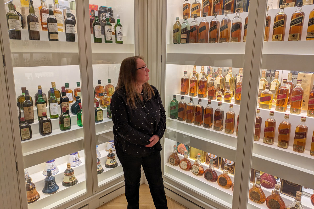 A woman stands surrounded by shelves full of whisky bottles