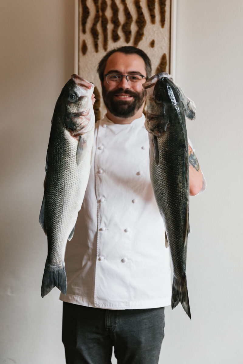 A bearded chef holds some large fish aloft
