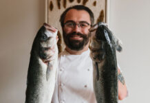 A bearded chef holds some large fish aloft