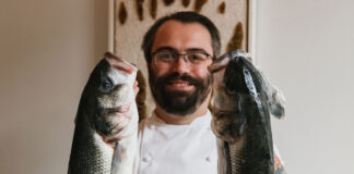 A bearded chef holds some large fish aloft