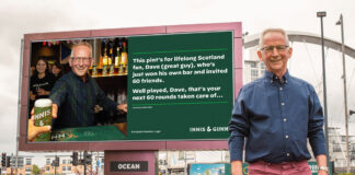 A middle-aged man stands in front of a billboard with his own face on it