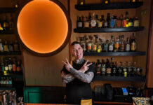A heavily tattooed bartender strikes a rock pose