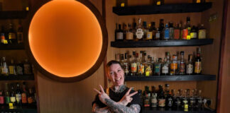 A heavily tattooed bartender strikes a rock pose