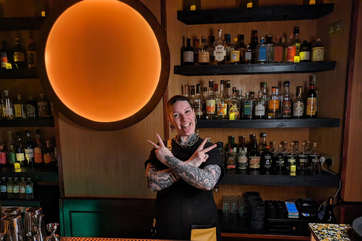 A heavily tattooed bartender strikes a rock pose