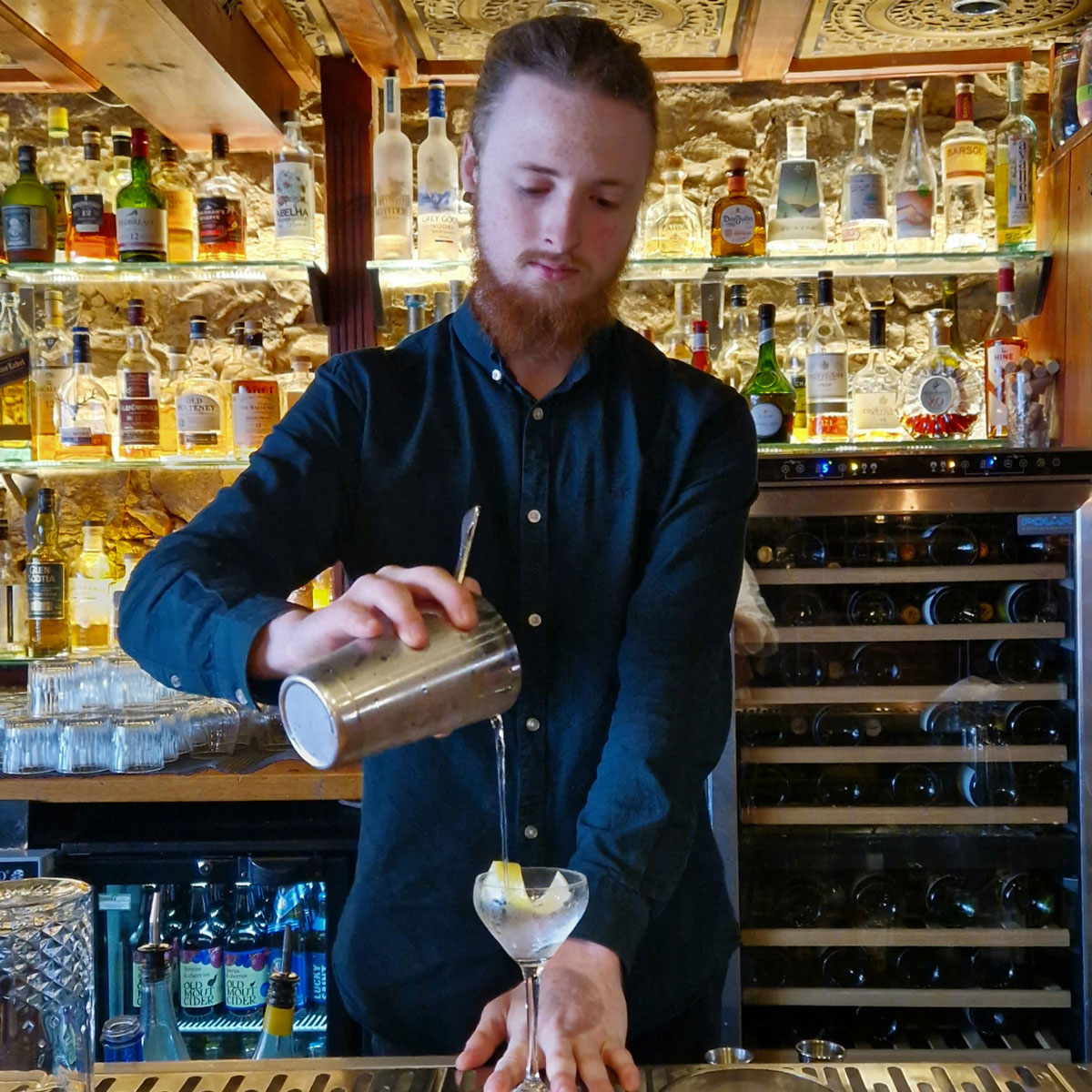 A young man with a beard pours a cocktail