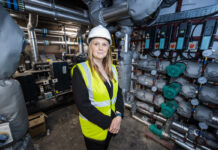 A blond lady stands in a pump room wearing a hard hat and high vis