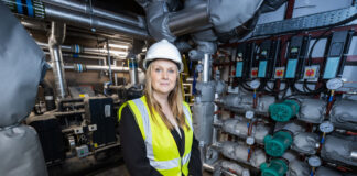 A blond lady stands in a pump room wearing a hard hat and high vis