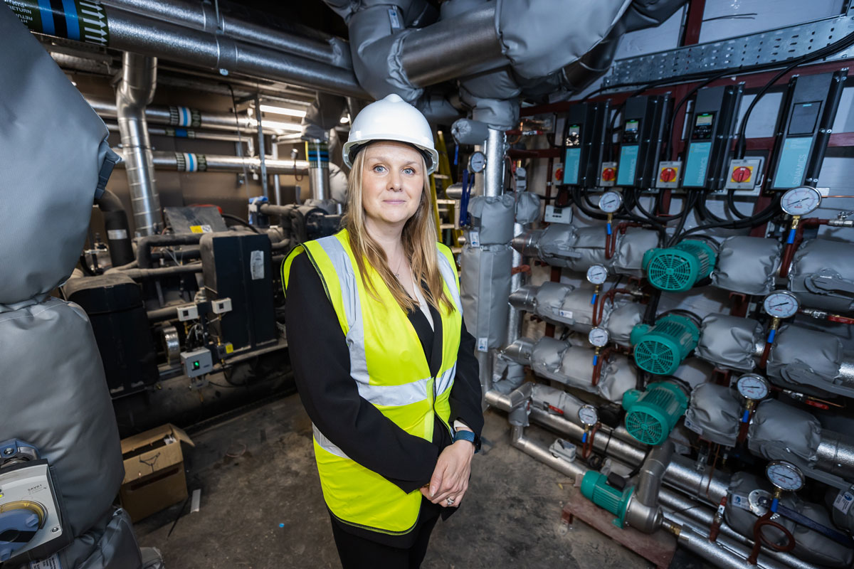 A blond lady stands in a pump room wearing a hard hat and high vis