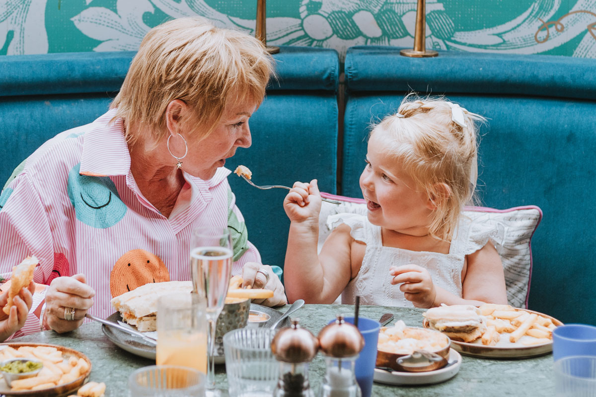 A grandmother eats food off a fork offered by her granddaughter