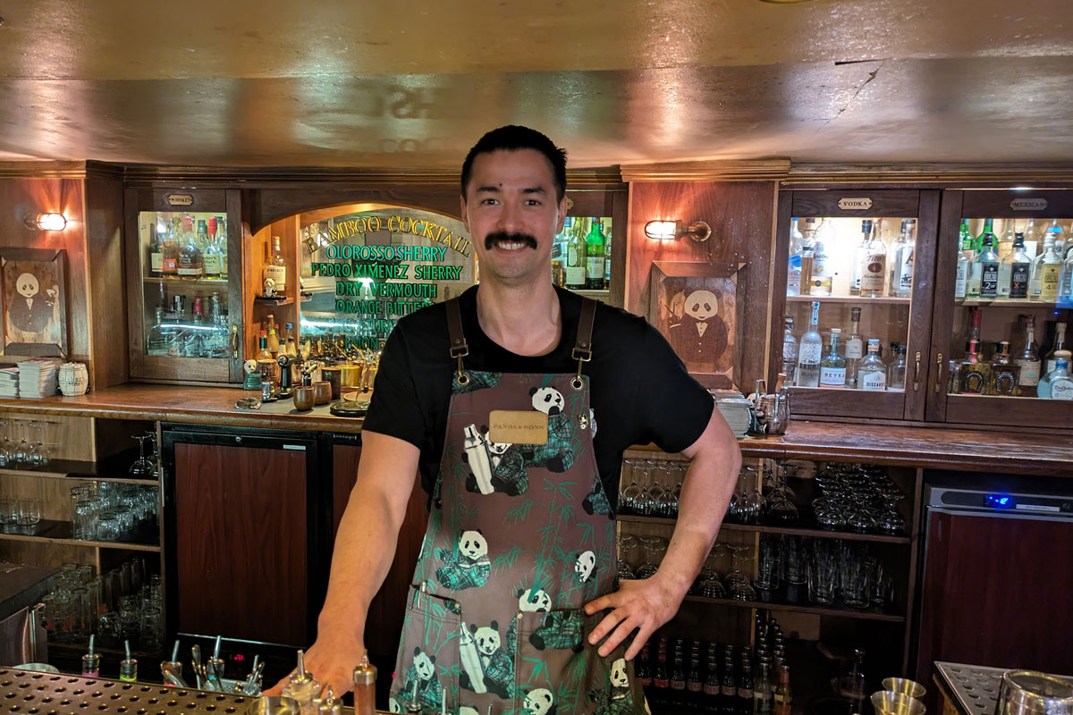 A bartender behind his bar, wearing a panda-themed apron