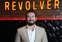 A bearded man stands in front of a neon sign