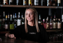 A young blonde woman serves behind a bar