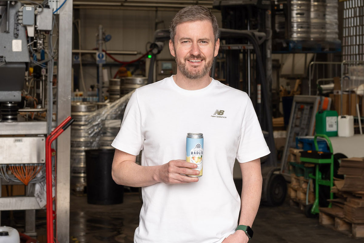 A casually dressed man smiles as he holds a can of beer