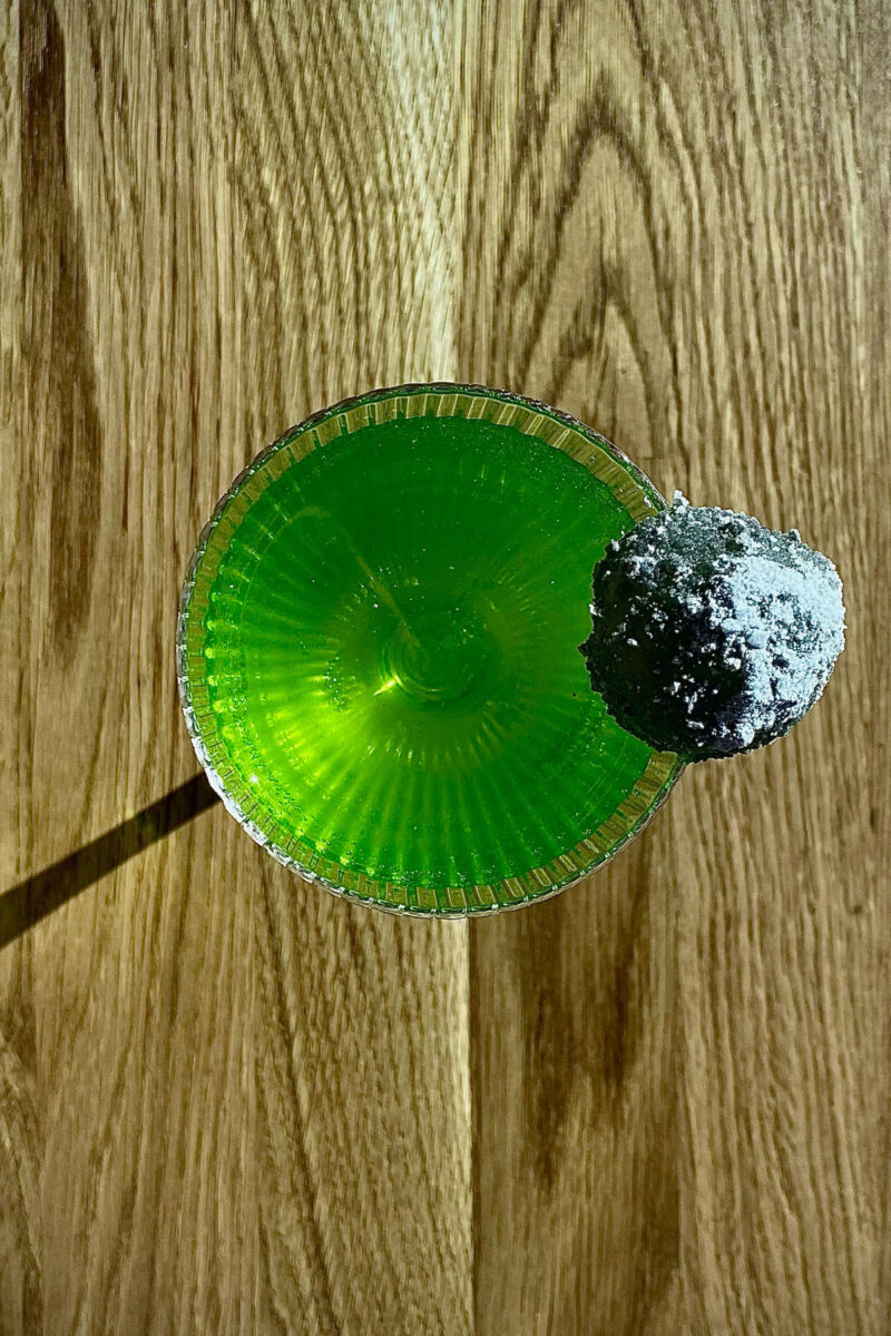 A bright green drink with a piece of space rock on the rim of the glass