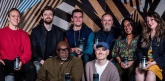 Six people sitting or standing around a nightclub table and two cans of lager