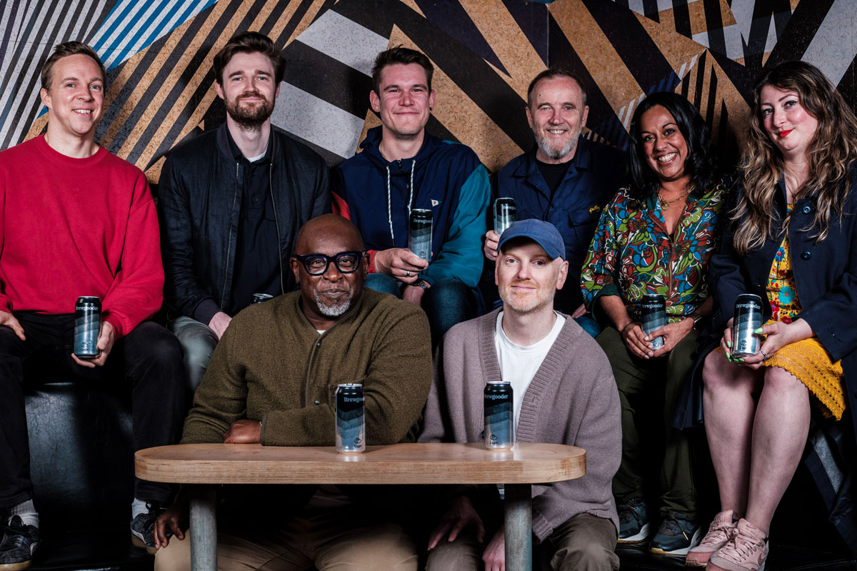 Six people sitting or standing around a nightclub table and two cans of lager