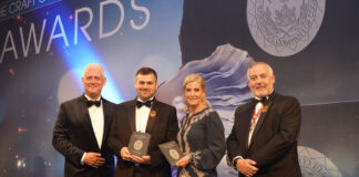 A well-dressed man receives an award from a well-dressed woman, while two well-dressed men look on