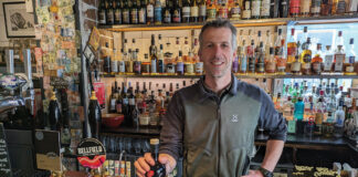 Chris Miles behind the bar of The Black Cat with a bottle of Pochle eau de vie