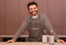 A young bearded man grins behind a bar