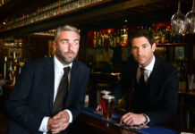 Two smartly dressed young men sit at a bar