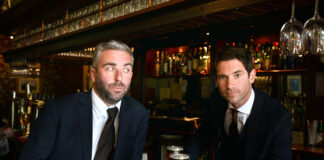 Two smartly dressed young men sit at a bar