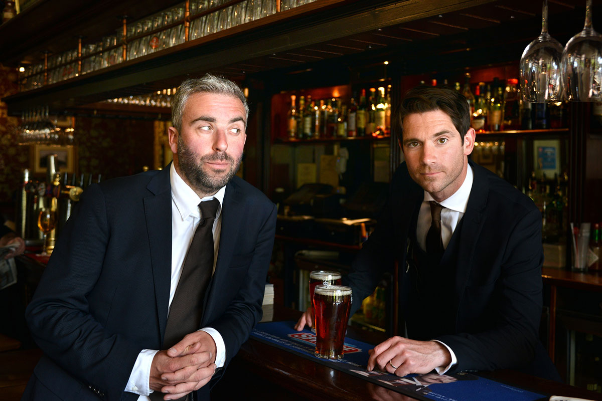 Two smartly dressed young men sit at a bar