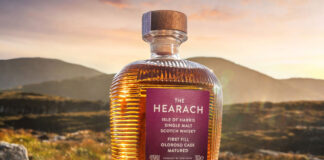 A single whisky bottle sits in the Scottish landscape
