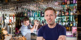 A young man sits smiling in front of a bar