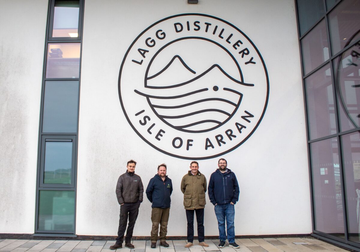 Four men stand in front a corporate logo on a wall